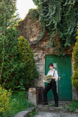 Elinde gazete olan güzel bir kız, beyaz gömlekli, siyah pantolonlu, yakın plan pantolon giyen.