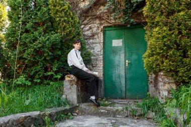 Elinde gazete olan güzel bir kız, beyaz gömlekli, siyah pantolonlu, yakın plan pantolon giyen.