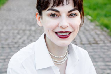 Beyaz tişörtlü, siyah pantolonlu, arka planında pantolon askısı olan yeşil çimenler olan güzel bir kız.