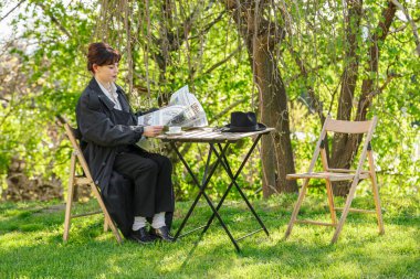 Güzel bir kız masada kahve içiyor, yağmurlukla, beyaz gömlekle, siyah pantolonla, yakın plan pantolon ile.