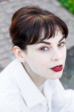 Beyaz tişörtlü, siyah pantolonlu, arka planında pantolon askısı olan yeşil çimenler olan güzel bir kız.