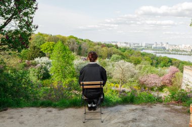 Güzel bir kız masada kahve içiyor, yağmurlukla, beyaz gömlekle, siyah pantolonla, yakın plan pantolon ile.