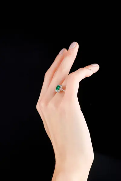 Beautiful female hand with gold ring with diamonds and emerald on black background close-up