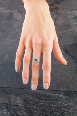 Altın yüzüklü, elmaslı güzel bir kadın eli ve yakın plan gri arkaplanlı bir deniz mavisi.