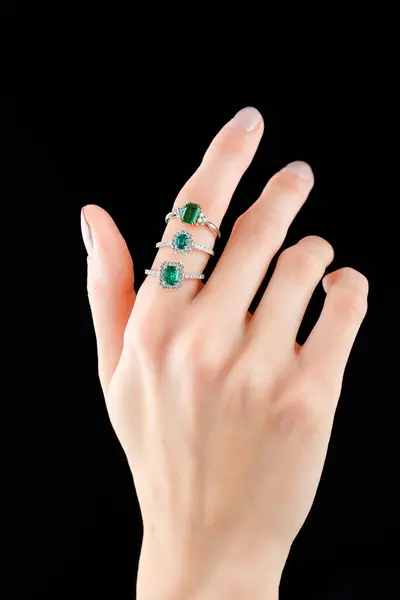 Beautiful female hand with gold ring with diamonds and emerald on black background close-up