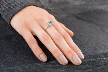 Altın yüzüklü, elmaslı güzel bir kadın eli ve yakın plan gri arkaplanlı bir deniz mavisi.