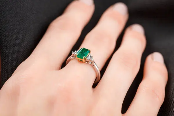 Beautiful female hand with gold ring with diamonds and emerald on gray background close-up