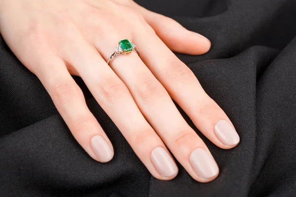 Beautiful female hand with gold ring with diamonds and emerald on gray background close-up
