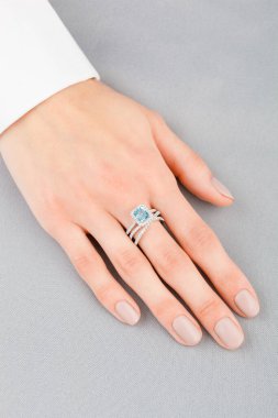 Altın yüzüklü, elmaslı güzel bir kadın eli ve yakın plan gri arkaplanlı bir deniz mavisi.