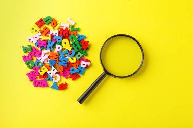 Alfabenin sarı arkaplanda büyüteçle kaplanmış renkli harfleri.