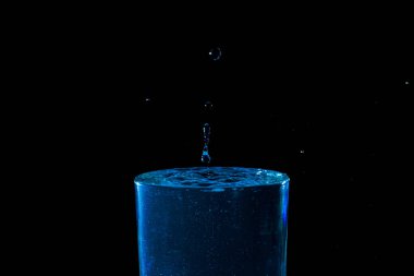 Su damlası düşüyor, makro sıçrama. Doğal ve karanlık bir arkaplanda yakın plan.