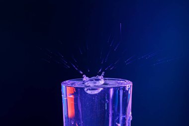 Su damlası düşüyor, makro sıçrama. Doğal ve karanlık bir arkaplanda yakın plan.