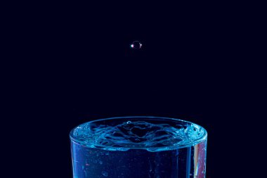 Su damlası düşüyor, makro sıçrama. Doğal ve karanlık bir arkaplanda yakın plan.