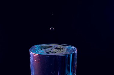 Su damlası düşüyor, makro sıçrama. Doğal ve karanlık bir arkaplanda yakın plan.