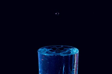 Su damlası düşüyor, makro sıçrama. Doğal ve karanlık bir arkaplanda yakın plan.