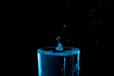 Su damlası düşüyor, makro sıçrama. Doğal ve karanlık bir arkaplanda yakın plan.