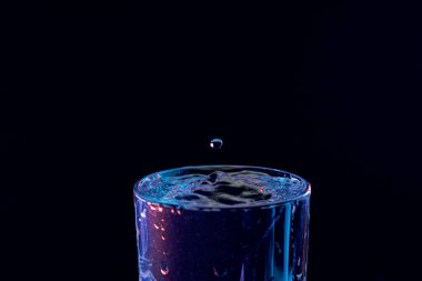 Su damlası düşüyor, makro sıçrama. Doğal ve karanlık bir arkaplanda yakın plan.