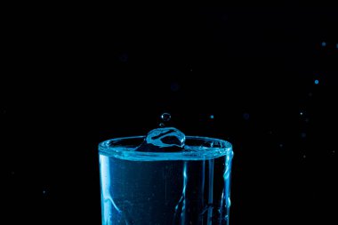 Su damlası düşüyor, makro sıçrama. Doğal ve karanlık bir arkaplanda yakın plan.