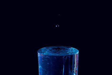 Su damlası düşüyor, makro sıçrama. Doğal ve karanlık bir arkaplanda yakın plan.