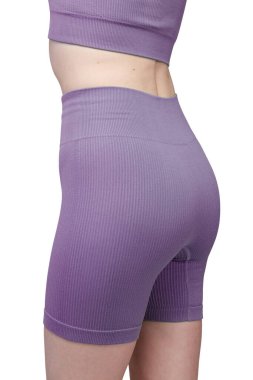 Formda bir kadının sırtından atölye çekiminde, gri çatallı, pürüzsüz spor şortu ve uyumlu spor sutyeni sergileniyor. Kumaş desenli bir örgü. Beyaz arka planda izole edilmiş. Spor giyim, spor giyim ve fitness programları için ideal.