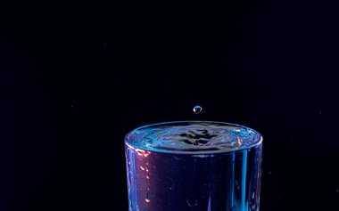 Su damlası düşüyor, makro sıçrama. Doğal ve karanlık bir arkaplanda yakın plan.