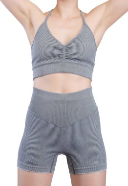 Stüdyoda, formda bir kadının kalçasını ve bacaklarını gösteren belden aşağısı. Gri, kaburgasız spor sutyen ve yüksek bel şort giyiyor. Kumaş desenli bir örgü. Beyaz arka planda izole edilmiş. Formda kalmak için ideal.