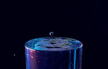 Su damlası düşüyor, makro sıçrama. Doğal ve karanlık bir arkaplanda yakın plan.