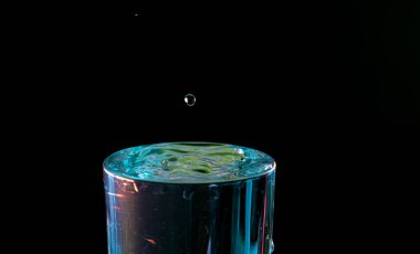 Su damlası düşüyor, makro sıçrama. Doğal ve karanlık bir arkaplanda yakın plan.