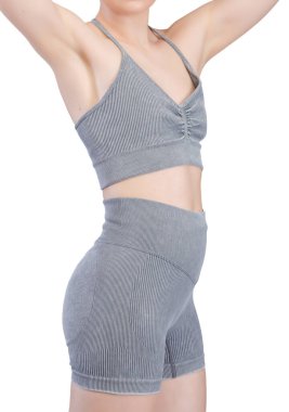 Stüdyoda, formda bir kadının kalçasını ve bacaklarını gösteren belden aşağısı. Gri, kaburgasız spor sutyen ve yüksek bel şort giyiyor. Kumaş desenli bir örgü. Beyaz arka planda izole edilmiş. Formda kalmak için ideal.