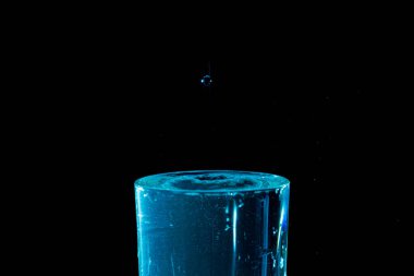 Su damlası düşüyor, makro sıçrama. Doğal ve karanlık bir arkaplanda yakın plan.