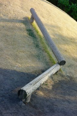 Parktaki bir nesne, çıplak toprak yığını üzerine dizayn edilmiş kütüklerin birleşimi..