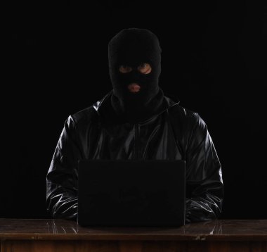 masked hacker with laptop at night