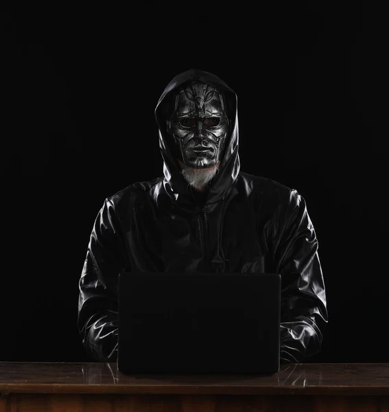 masked hacker with laptop at night