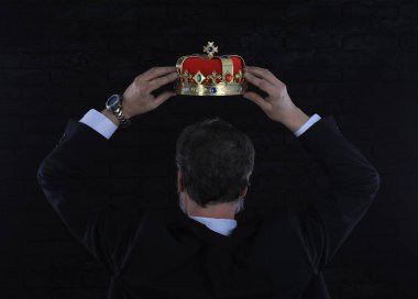 İş adamı taç takıyor, siyah arka plan.