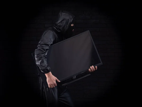 stock image masked thief with tv on black background