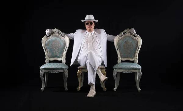rich gentleman in a white suit sits on a chair, black studio background