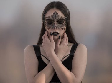 Siyah makyajlı, siyah bir karnaval maskesi takmış, parlak siyah ruj ve oje sürmüş, klasik tiyatro tarzı.