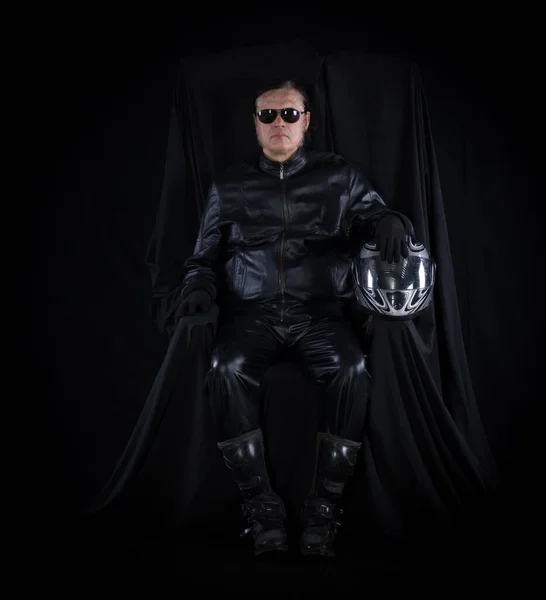 portrait of a biker in a helmet on a chair on a black background
