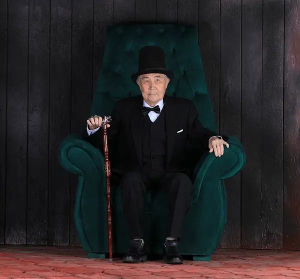 Reicher Alter Mann Auf Einem Stuhl Vor Schwarzem Hintergrund — Stockfoto