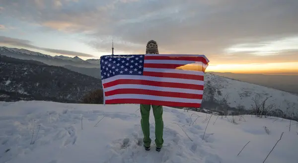 man in the mountains with an American flag in winter