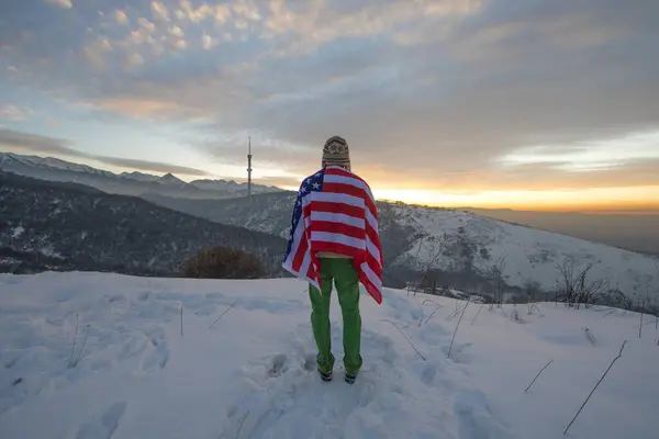 man in the mountains with an American flag in winter