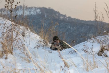 Keskin nişancı, silahlı asker çalıların arasında saklanıyor, kış.