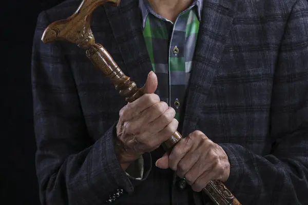 hands of an old man with a crutch on a black background
