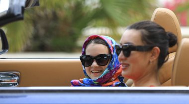 Güzel, zengin, esmer, kırmızı elbiseli kız bir arabanın direksiyonunda.