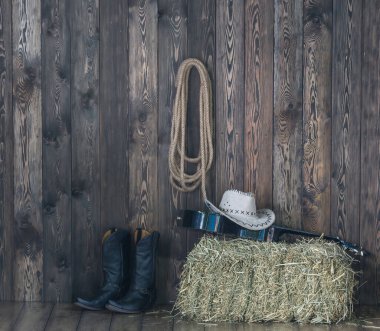 Kovboy şapkası, çizmeler ve gitar eski bir ahırın arka planında..