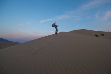 Gün batımında kumulda elbise giymiş genç bir kız