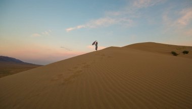 Gün batımında kumulda elbise giymiş genç bir kız
