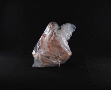 Çıplak bir adam siyah bir arka planda plastik bir çantada boğuluyor.
