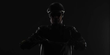 Siyah arka planda siyah elbiseli bir motorcunun portresi