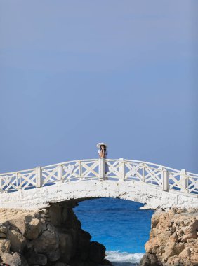 Güzel esmer kadın, deniz kenarında köprüde yürüyor.